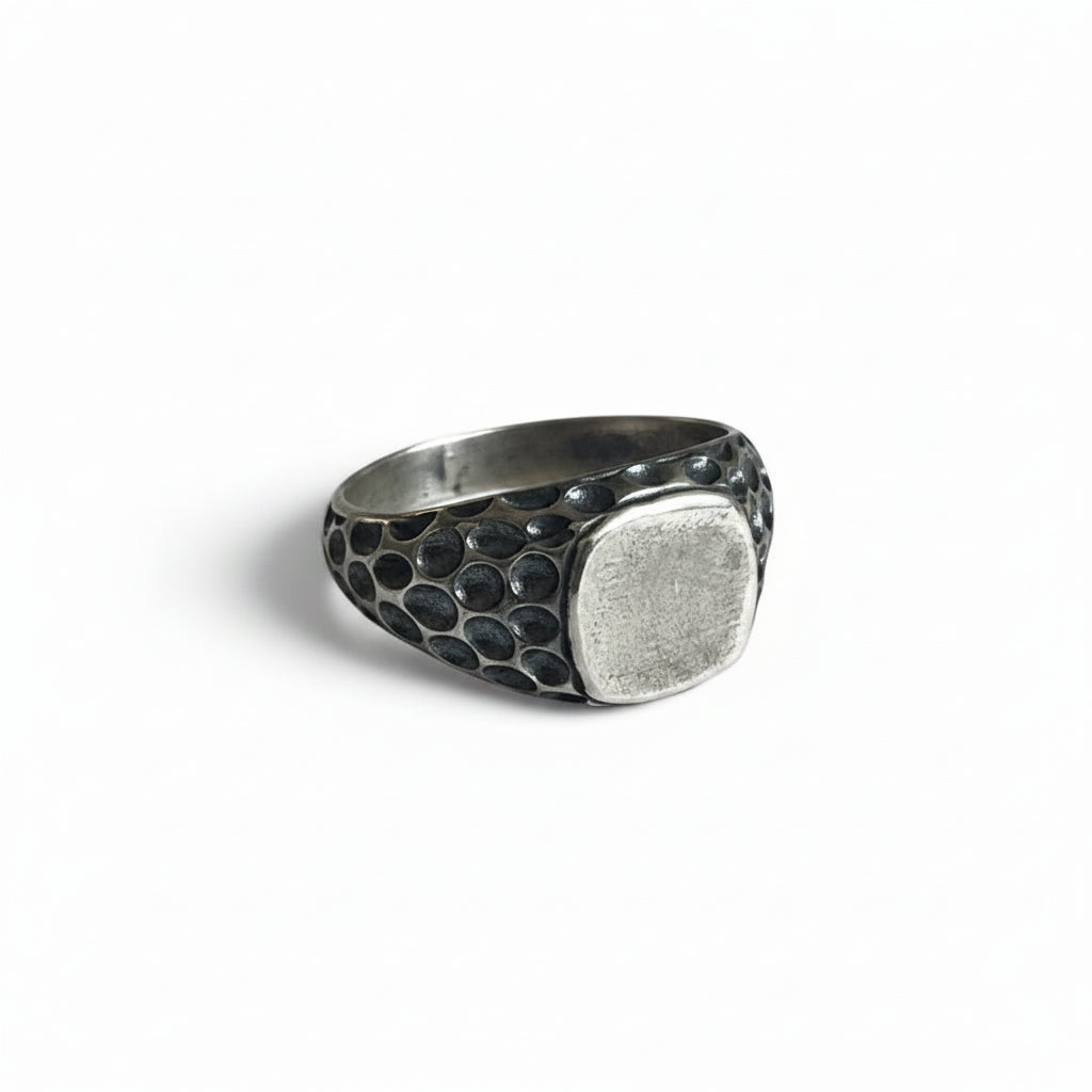 A silver-toned signet ring with a hammered, textured band and a smooth, flat oval face, shown on a plain white background.