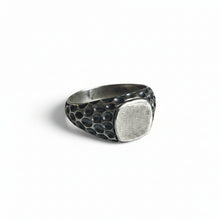 A silver-toned signet ring with a hammered, textured band and a smooth, flat oval face, shown on a plain white background.