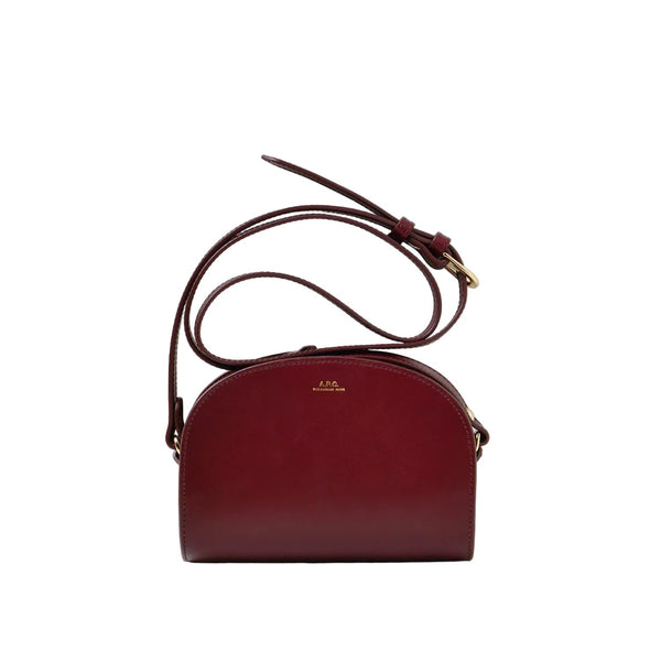 A burgundy leather dome-shaped crossbody bag with a matching adjustable shoulder strap and gold-tone hardware, displayed against a clean white studio background.