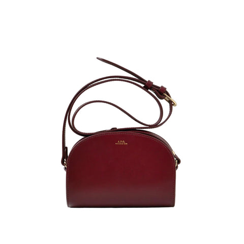 A burgundy leather dome-shaped crossbody bag with a matching adjustable shoulder strap and gold-tone hardware, displayed against a clean white studio background.